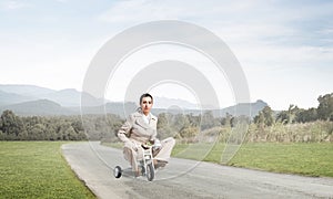 Caucasian woman riding kid`s bicycle on road
