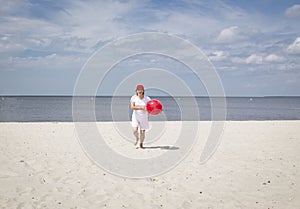 Caucasian woman running on the sandy beach with red ball.