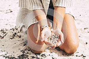 Caucasian woman on the sand at the beach holding and showing a lot of little marine shells under the sunny day - tourism and