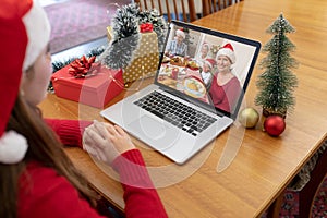 Caucasian woman in santa hat making christmas laptop video call with smiling family at dinner table