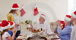 Caucasian woman in santa hat serving food to whole family