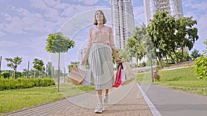 Caucasian woman with shot hair holding shopping bags and walking on a road in a park
