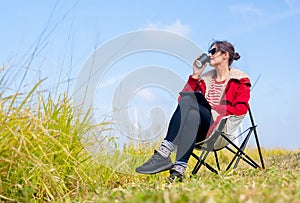 Caucasian woman sit on chair near meadow with blue sky and drink coffee with relax action in front of wind turbines or windmill