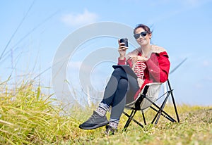 Caucasian woman sit on chair near meadow with blue sky and wind turbines or windmill on the back and she also hold a cup of coffee