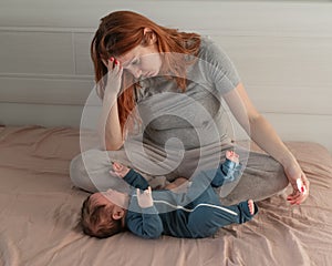 A Caucasian woman sits on a bed next to a crying baby. Postpartum depression.