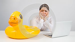 Caucasian woman sits at a table with a laptop and an inflatable duck on a white background. Office worker dreaming of