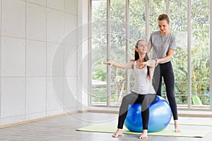 Caucasian woman sitting and balancing on exercise ball with trainer. fitness, sport, training and people concept
