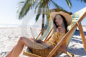 Caucasian woman sitting on a deck chair and using a laptop at the beach