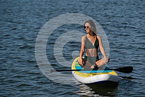 Caucasian woman sitting in lotus position on SUP board on the lake. Summer sports.