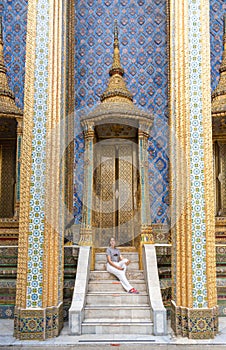 Caucasian woman sitting on the marble stairs at the Temple of the Emerald Buddha. Bangkok, Thailand
