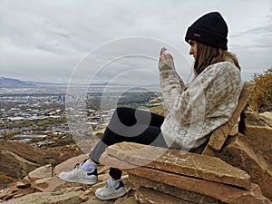 Caucasian woman sitting on a rocky sofa taking a photo to the view from Living Room Trailhead hike