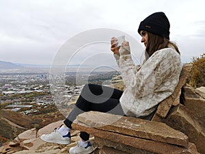 Caucasian woman sitting on a rocky sofa with a winter hat taking a photo to the view from Living Room Trailhead hike