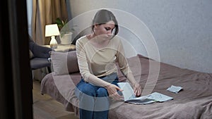 A Caucasian woman is sitting on a sofa in a room, looking at documents and tearing up paper. Despair and depression