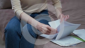 A Caucasian woman is sitting on a sofa in a room and looking at paper documents