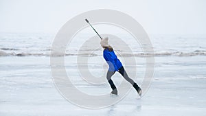 A caucasian woman is skating on a frozen lake holding a selfie stick in her hands. The figure skater films her skating.