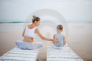 Caucasian woman with son practicing yoga at seashore of tropic ocean