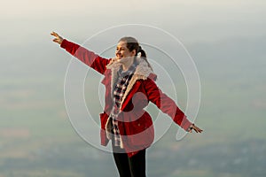 Caucasian woman stand near cliff with background of grass field and rural village area in view on the mountain with warm light of
