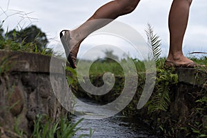 Caucasian woman step over the water ditch. Se has an active vacation in asia and goes for a walk