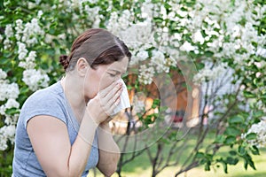 Caucasian woman suffers from allergies and blows her nose into a napkin while walking in the park.