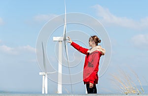 Caucasian woman with sun glasses touch action with same position of wind turbine or windmill with blue sky in concept of green