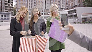 Caucasian woman taking photoes of her three friends with shopping bags. Four fashion women resting after shopping. Girls