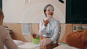 Caucasian woman teacher in elementary school teach children class ask question kids rise hands answer in classroom