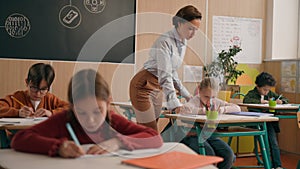 Caucasian woman teacher in elementary school teach children class kids writing task in classroom knowledge studying