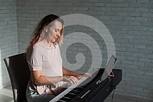 Caucasian woman teaches playing the electric piano online on a digital tablet