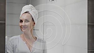 Caucasian woman with a towel on her head in front of a mirror in the bathroom. Face wash, skincare, wellness