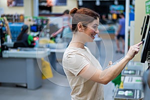 Caucasian woman uses a self-checkout counter. Self-purchase of groceries in the supermarket without a seller