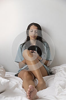 Caucasian woman using cell phone while chatting on white-sheeted bed in the bedroom