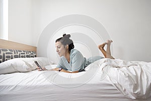 Caucasian woman using cell phone while chatting on white-sheeted bed in the bedroom