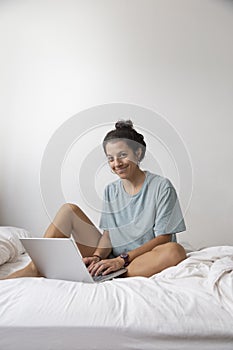 Caucasian woman using laptop computer on white-sheeted bed