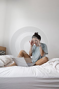 Caucasian woman using laptop computer on white-sheeted bed