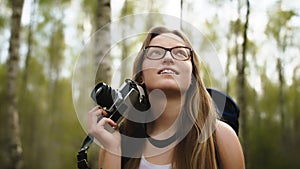 Caucasian woman with vintage camera enjoying holiday in the nature. Backpacker in the forest. Lens flare.