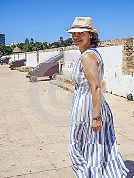 A Caucasian woman walking along an antique Latinamerican marina promenade