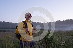 Caucasian woman walking in field alone. Girl in sport clothes hiking with backpack.