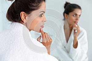 Caucasian woman wearing bathrobe standing in bathroom and lookig in mirror