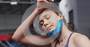 Caucasian woman wearing lowered face mask exercising at gym