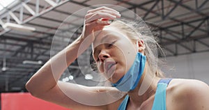 Caucasian woman wearing lowered face mask wiping brow at gym