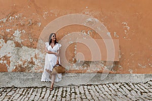 Caucasian woman wearing white drees standing in front of orange weathered wall