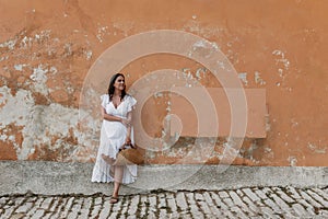 Caucasian woman wearing white drees standing in front of orange weathered wall