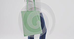Caucasian woman wearing white hoodie holding green bag on white background, copy space, slow motion