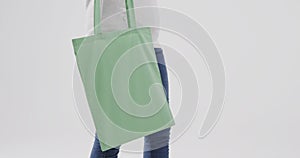 Caucasian woman wearing white hoodie holding green bag on white background, copy space, slow motion