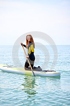 Caucasian woman in wetsuit working out with stand up paddle board on water