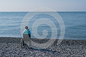 Caucasian woman in a wheelchair on a pebble beach by the sea.