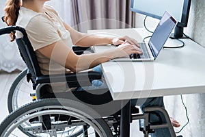 Caucasian woman in a wheelchair typing with a laptop from home. Remote work for people with disabilities.