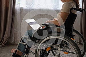 Caucasian woman in a wheelchair typing with a laptop from home. Remote work for people with disabilities.