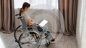 Caucasian woman in a wheelchair typing with a laptop from home. Remote work for people with disabilities.