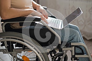 Caucasian woman in a wheelchair typing with a laptop from home. Remote work for people with disabilities.